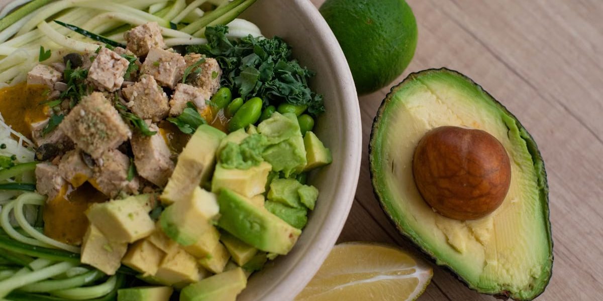 Delicious vegan bowl with zoodles, avocado, tofu, and greens on a wooden table.