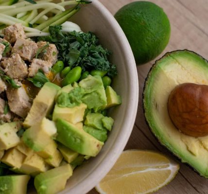 Delicious vegan bowl with zoodles, avocado, tofu, and greens on a wooden table.