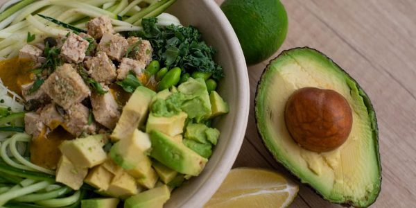 Delicious vegan bowl with zoodles, avocado, tofu, and greens on a wooden table.