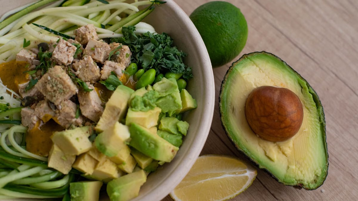 Delicious vegan bowl with zoodles, avocado, tofu, and greens on a wooden table.